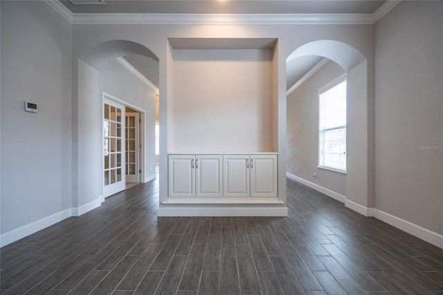 unfurnished room featuring ornamental molding, arched walkways, dark wood finished floors, and baseboards