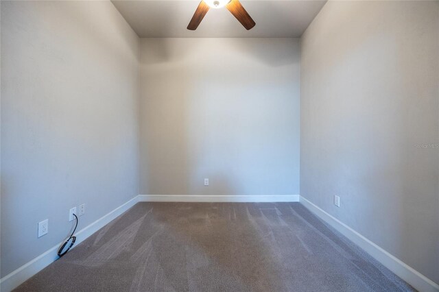 empty room with dark colored carpet, a ceiling fan, and baseboards