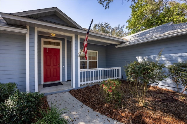 doorway to property featuring a porch and roof with shingles