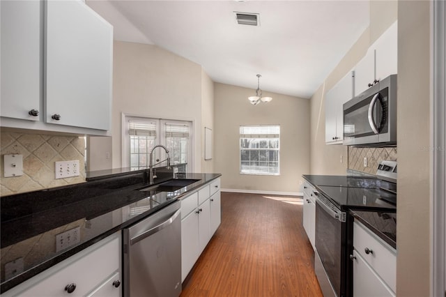 kitchen featuring stainless steel appliances, vaulted ceiling, white cabinets, and a sink