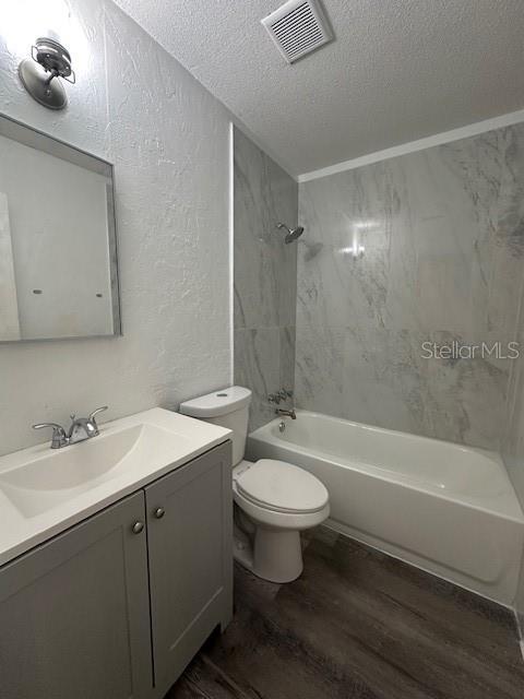 bathroom with visible vents, a textured wall, wood finished floors, a textured ceiling, and washtub / shower combination