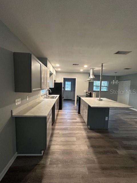 kitchen featuring black range with electric stovetop, a sink, wood finished floors, baseboards, and light countertops