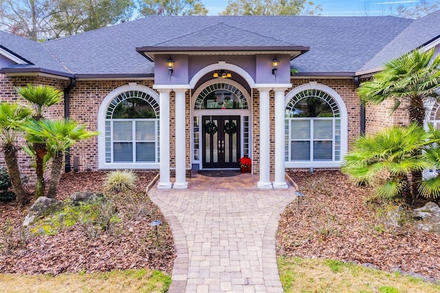 property entrance featuring french doors, roof with shingles, and brick siding