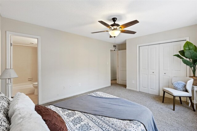 bedroom with ensuite bathroom, light colored carpet, a ceiling fan, baseboards, and a closet