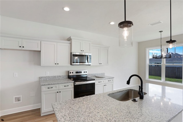 kitchen with a center island with sink, stainless steel appliances, visible vents, white cabinetry, and a sink