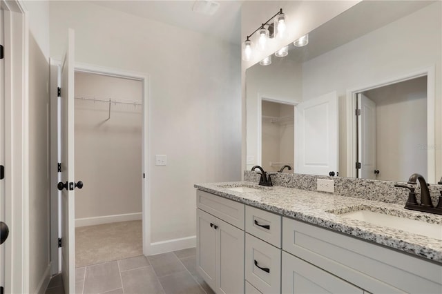 full bath with double vanity, a sink, a walk in closet, and baseboards