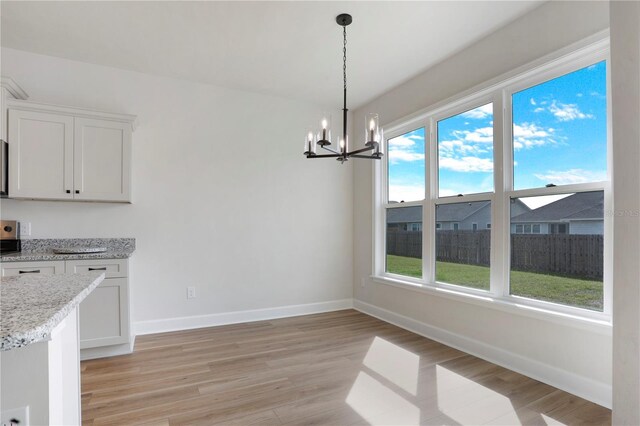 unfurnished dining area with light wood-type flooring, baseboards, and an inviting chandelier