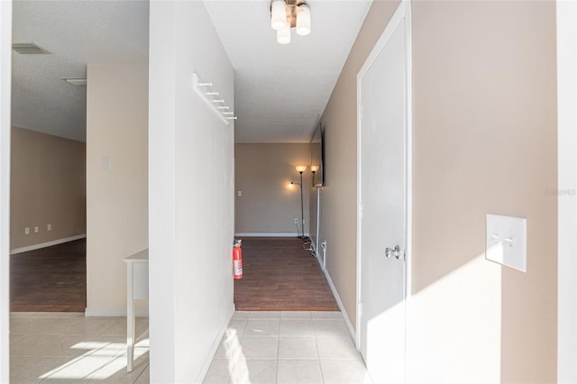 corridor with baseboards, visible vents, a textured ceiling, and light tile patterned flooring