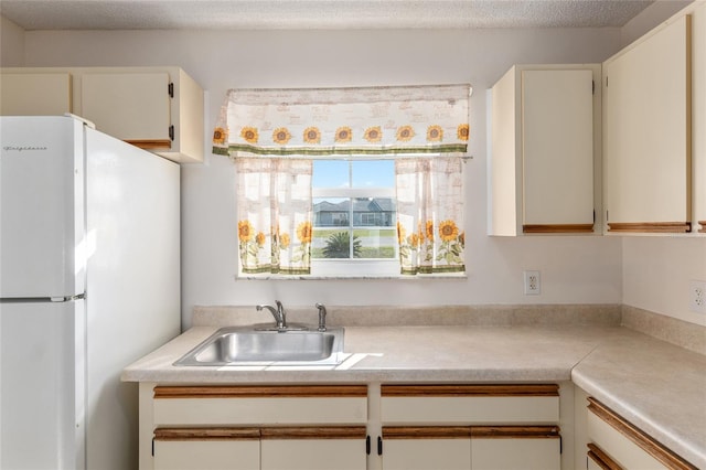 kitchen with light countertops, freestanding refrigerator, white cabinetry, a sink, and a textured ceiling