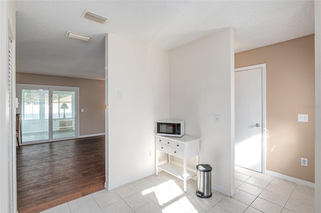 interior space featuring light tile patterned floors, a textured ceiling, visible vents, and baseboards