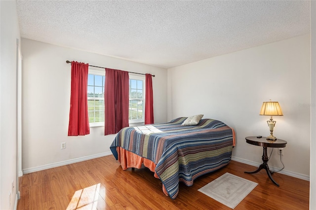 bedroom featuring a textured ceiling, baseboards, and wood finished floors