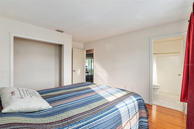 bedroom with visible vents, a textured ceiling, ensuite bathroom, and wood finished floors