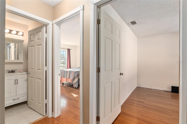 hall featuring light wood-type flooring, visible vents, a textured ceiling, and baseboards