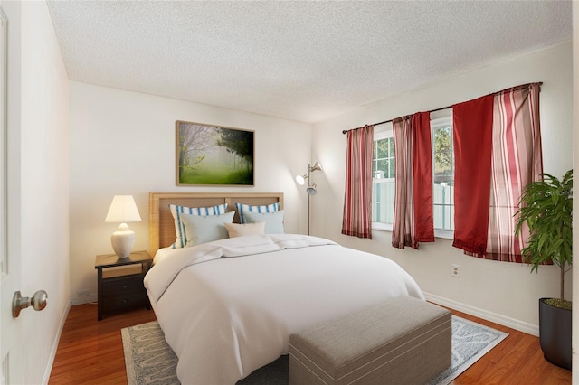 bedroom with a textured ceiling, wood finished floors, and baseboards