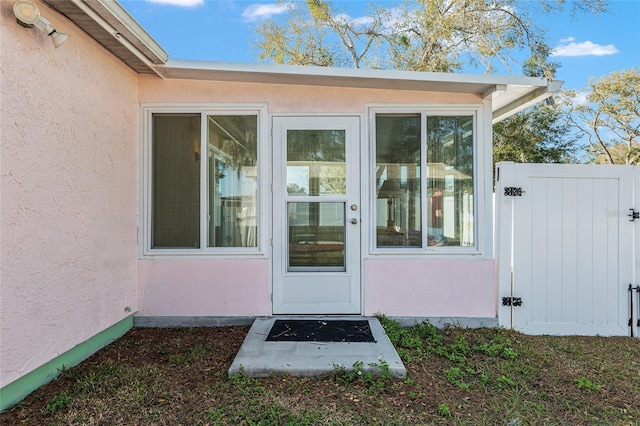 property entrance featuring a gate, fence, and stucco siding