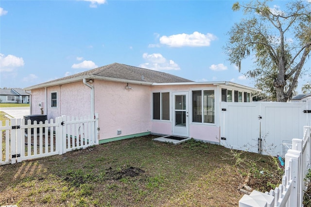 rear view of house with a lawn, a sunroom, fence private yard, a gate, and stucco siding