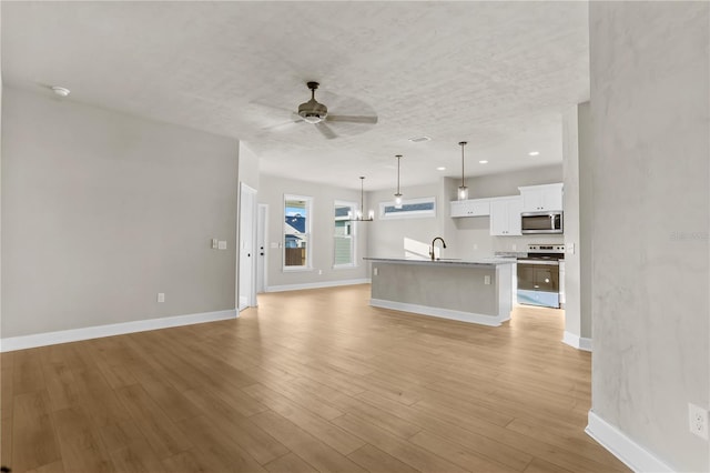 unfurnished living room with light wood finished floors, baseboards, a textured ceiling, a sink, and ceiling fan with notable chandelier