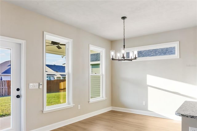 unfurnished dining area with a wealth of natural light, light wood-type flooring, baseboards, and an inviting chandelier