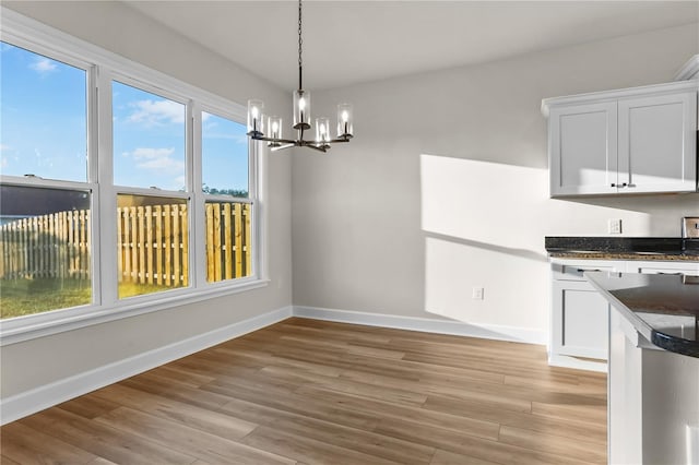 unfurnished dining area with light wood-type flooring, an inviting chandelier, and baseboards