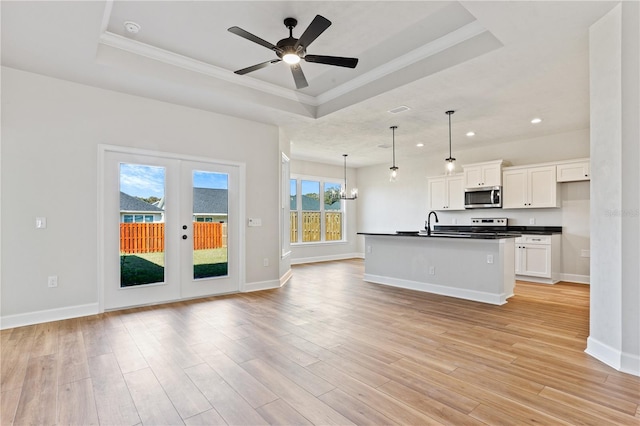 kitchen with light wood finished floors, stainless steel appliances, dark countertops, a raised ceiling, and open floor plan