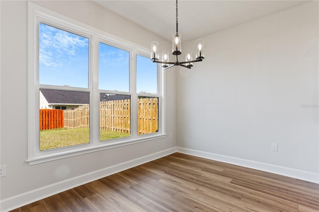 unfurnished dining area featuring an inviting chandelier, baseboards, and wood finished floors