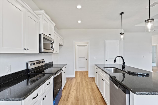 kitchen with stainless steel appliances, white cabinets, a kitchen island with sink, a sink, and light wood-type flooring