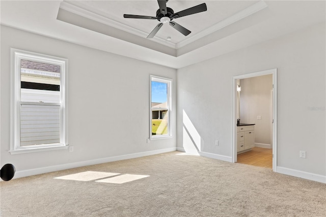 unfurnished bedroom with light carpet, baseboards, a raised ceiling, ensuite bathroom, and crown molding