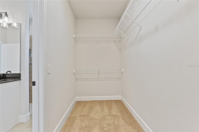 walk in closet with light carpet and a sink