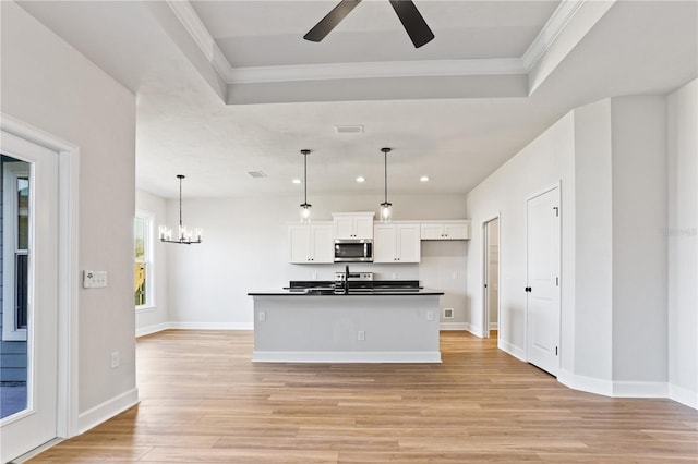 kitchen with dark countertops, stainless steel microwave, ornamental molding, light wood-style floors, and white cabinetry