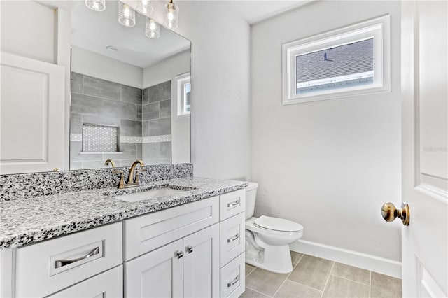 bathroom featuring tile patterned flooring, toilet, vanity, baseboards, and a tile shower