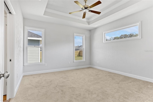 empty room featuring a tray ceiling, carpet, crown molding, ceiling fan, and baseboards