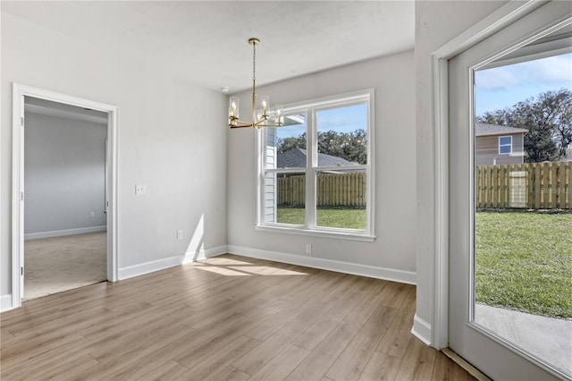 unfurnished dining area with baseboards, light wood finished floors, and a notable chandelier