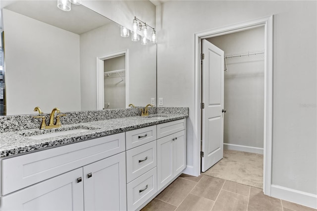 bathroom with a sink, a spacious closet, baseboards, and double vanity