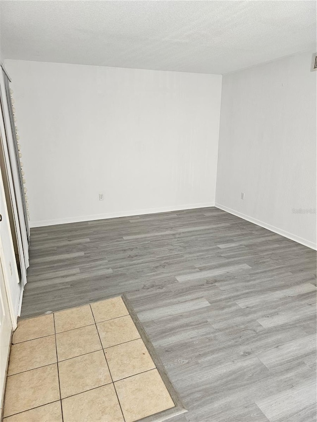 unfurnished room featuring a textured ceiling, wood finished floors, visible vents, and baseboards