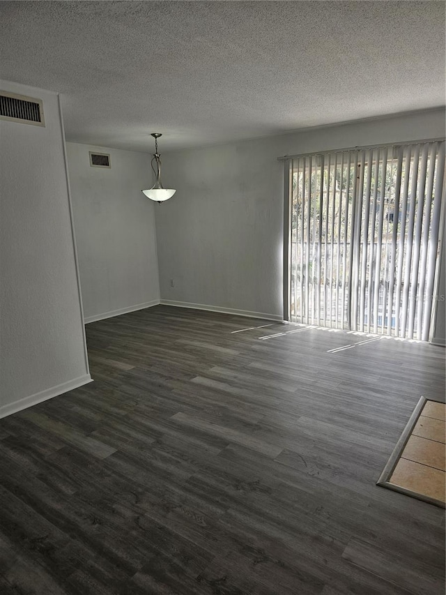 empty room with a textured ceiling, dark wood-type flooring, visible vents, and baseboards