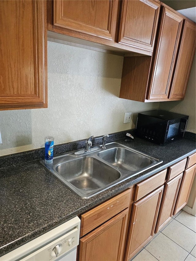 kitchen featuring dark countertops, light tile patterned flooring, white dishwasher, a sink, and black microwave