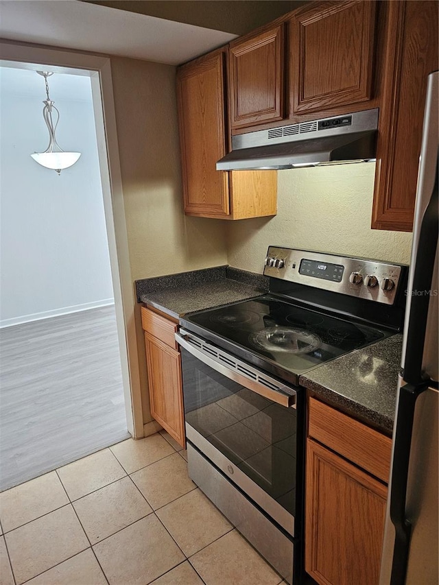 kitchen featuring dark countertops, freestanding refrigerator, light tile patterned flooring, stainless steel range with electric stovetop, and under cabinet range hood