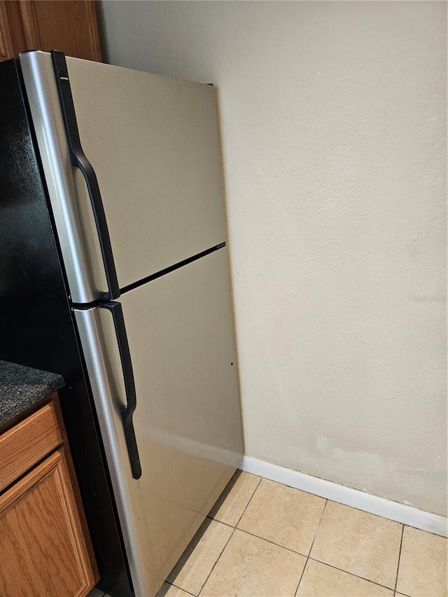 kitchen featuring light tile patterned floors, baseboards, brown cabinetry, and freestanding refrigerator