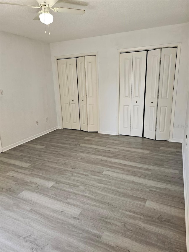 unfurnished bedroom with wood finished floors, two closets, a ceiling fan, and baseboards