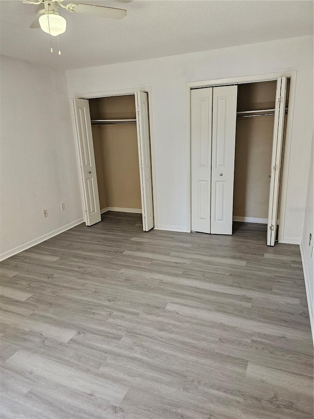 unfurnished bedroom with a textured ceiling, wood finished floors, a ceiling fan, baseboards, and two closets