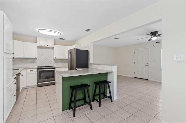 kitchen featuring a peninsula, stainless steel appliances, a kitchen bar, backsplash, and light tile patterned flooring