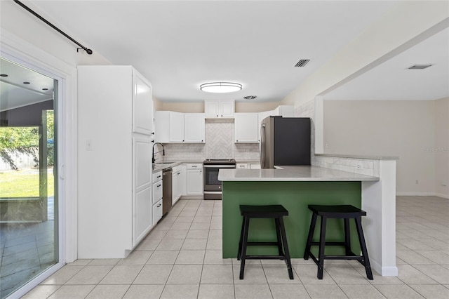 kitchen featuring light tile patterned floors, appliances with stainless steel finishes, a kitchen breakfast bar, a peninsula, and backsplash