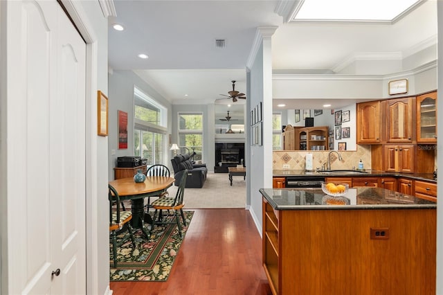 kitchen featuring a fireplace, a sink, decorative backsplash, brown cabinetry, and crown molding