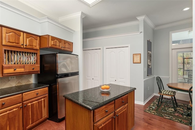 kitchen featuring brown cabinets, dark wood-style flooring, a center island, freestanding refrigerator, and crown molding