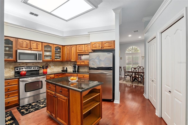 kitchen with appliances with stainless steel finishes, dark countertops, brown cabinets, and visible vents