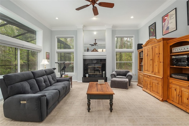 living area with light colored carpet, a ceiling fan, baseboards, ornamental molding, and a glass covered fireplace