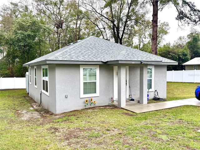 back of property with roof with shingles, fence, a lawn, and stucco siding