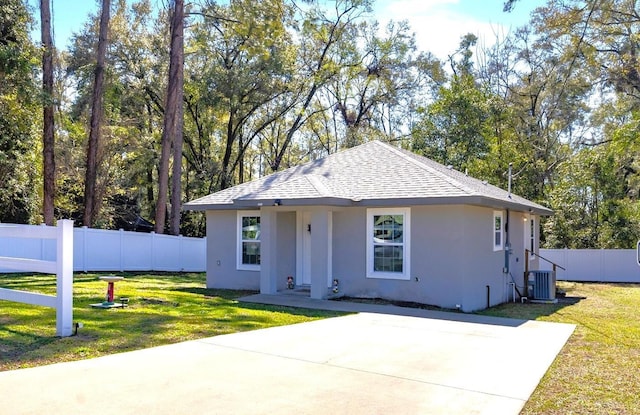 bungalow-style house featuring a shingled roof, central AC unit, fence, a front yard, and stucco siding