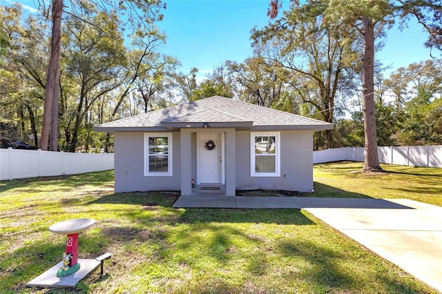 view of front of home featuring a shingled roof, fence, a front lawn, and stucco siding