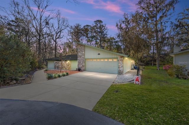 view of front facade with a garage, stone siding, driveway, board and batten siding, and a front yard